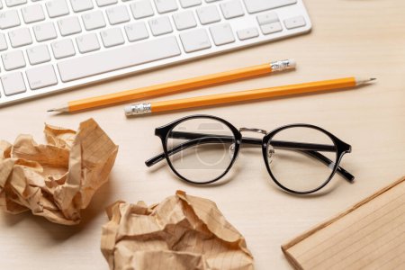 Photo for Top view of blank notepad, keyboard, eyeglasses and crumpled papers on desk, depicting unsuccessful attempts at writing - Royalty Free Image