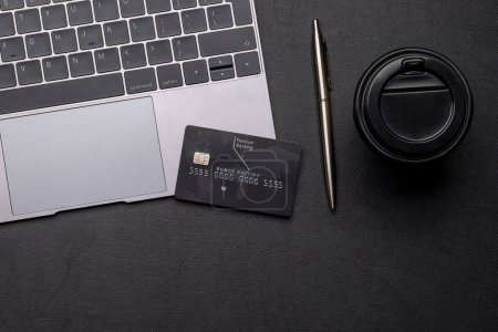 Téléchargez les photos : Carte de crédit noire sur la table de bureau avec ordinateur portable et tasse à café. Pose plate avec espace de copie. Concept de Premium Banking - en image libre de droit