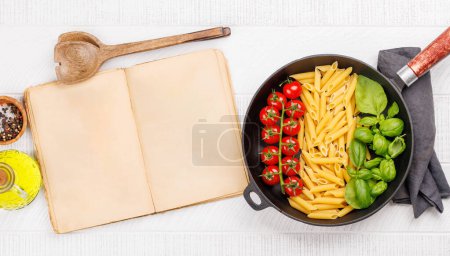 Téléchargez les photos : Une représentation vibrante du drapeau italien fait avec des pâtes, du basilic et des tomates, magnifiquement présenté dans une poêle à frire, et page de livre de cuisine pour votre recette. Pose plate avec espace de copie - en image libre de droit