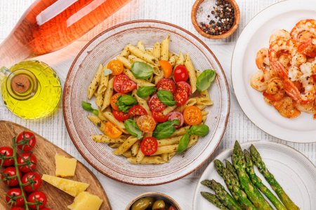 Téléchargez les photos : Assiette délicieuse de pâtes italiennes ornée de tomates fraîches et de feuilles de basilic aromatiques, d'asperges grillées et de crevettes. Pose plate - en image libre de droit
