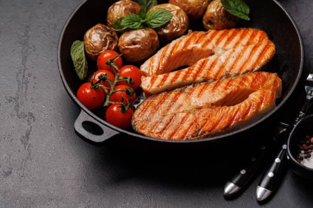 Photo for Grilled salmon steaks and potatoes sizzling in a frying pan - Royalty Free Image