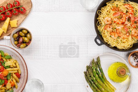 Téléchargez les photos : Assiette délicieuse de pâtes italiennes ornée de tomates fraîches et de feuilles de basilic aromatiques, d'asperges grillées et d'une poêle à pâtes aux crevettes. Pose plate avec espace de copie - en image libre de droit