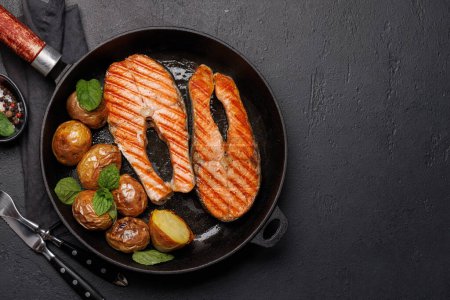 Téléchargez les photos : Des steaks de saumon grillés et des pommes de terre dans une poêle, un délice appétissant. Pose plate avec espace de copie - en image libre de droit