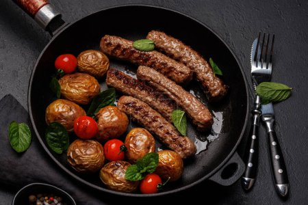 Photo for Delicious grilled sausages and potatoes in a sizzling frying pan. Flat lay - Royalty Free Image