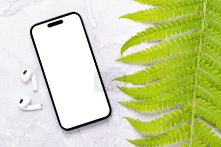 Photo for Smartphone with blank screen on a table surrounded by green nature leaves, perfect design mockup - Royalty Free Image