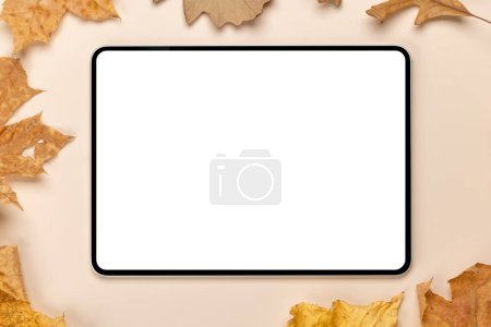 Téléchargez les photos : Tablette avec écran blanc sur une table entourée de feuilles de nature d'automne, maquette design parfaite - en image libre de droit
