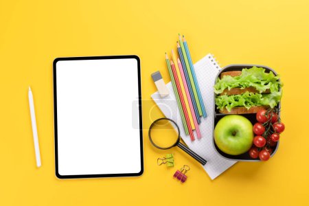 Photo for Tablet with blank screen, school supplies, stationery, and lunch box on yellow background. Education and nutrition. Flat lay with blank space for your text or app - Royalty Free Image