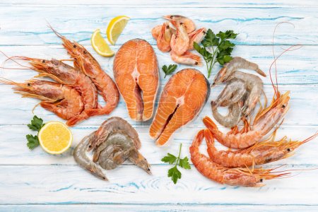 Photo for A top view of fresh seafood such as shrimp, langoustines and trout steaks. Flat lay on blue wooden table - Royalty Free Image