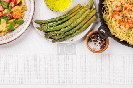 Photo for A delectable plate of Italian pasta adorned with fresh tomatoes and aromatic basil leaves, grilled asparagus and frying pan of pasta with prawns. Flat lay with copy space - Royalty Free Image