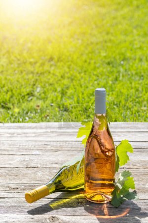 Foto de Botellas de vino blanco y rosa en una mesa de jardín al aire libre, preparando el escenario para una deliciosa fiesta de verano. Con espacio de copia - Imagen libre de derechos