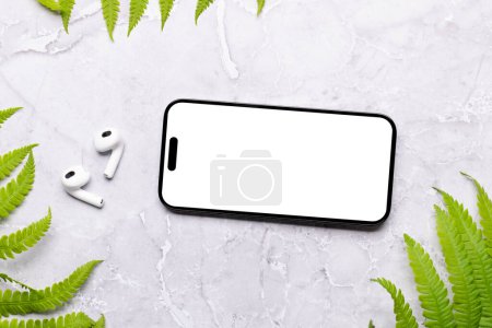 Foto de Smartphone con pantalla en blanco en una mesa rodeada de hojas verdes de la naturaleza, maqueta de diseño perfecto - Imagen libre de derechos