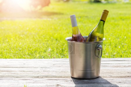 Foto de Botellas de vino blanco y rosa en cubo de hielo en una mesa de jardín al aire libre, preparando el escenario para una deliciosa fiesta de verano. Con espacio de copia - Imagen libre de derechos