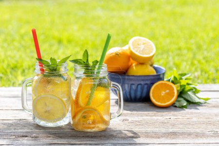 Foto de Refrescante limonada casera servida en una mesa de jardín al aire libre. Bebida fría de verano con cítricos frescos y menta de jardín - Imagen libre de derechos