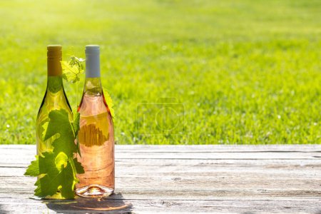Foto de Botellas de vino blanco y rosa en una mesa de jardín al aire libre, preparando el escenario para una deliciosa fiesta de verano. Con espacio de copia - Imagen libre de derechos
