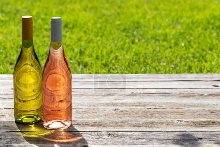 Téléchargez les photos : Bouteilles de vin blanc et rose sur une table de jardin en plein air, préparant le terrain pour une délicieuse fête d'été. Avec espace de copie - en image libre de droit