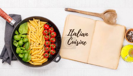 Téléchargez les photos : Une représentation vibrante du drapeau italien fait avec des pâtes, du basilic et des tomates, magnifiquement présenté dans une poêle et un livre de cuisine. Pose plate avec espace de copie - en image libre de droit
