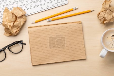 Photo for Top view of blank notepad, keyboard, coffee cup, eyeglasses and crumpled papers on desk, depicting unsuccessful attempts at writing - Royalty Free Image