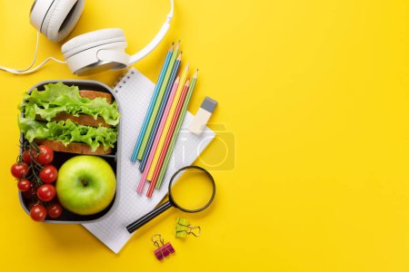 Foto de School supplies, stationery, and lunch box on yellow background. Education and nutrition. Flat lay with blank space - Imagen libre de derechos