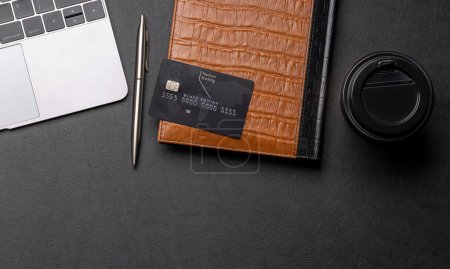 Foto de Tarjeta de crédito negra en la mesa de la oficina con ordenador portátil y taza de café. Piso con espacio de copia. Concepto bancario premium - Imagen libre de derechos