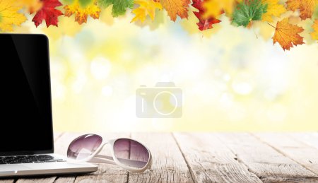 Téléchargez les photos : Ordinateur portable et lunettes de soleil sur une table en bois devant le décor d'automne. Travail et voyages ou concept d'entreprise à distance - en image libre de droit