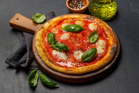 Foto de Pizza de margarita casera, cubierta con tomates frescos, queso mozzarella y hojas aromáticas de albahaca - Imagen libre de derechos