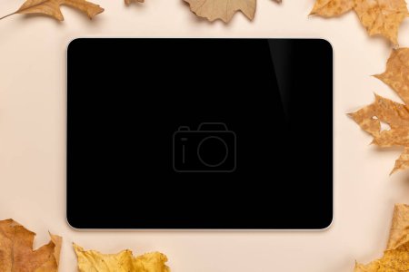 Foto de Tableta con pantalla en blanco en una mesa rodeada de hojas naturales de otoño, maqueta de diseño perfecto - Imagen libre de derechos