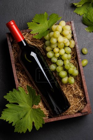 Téléchargez les photos : Une bouteille de vin rouge et des raisins frais, présentés dans une boîte en bois rustique. Pose plate - en image libre de droit