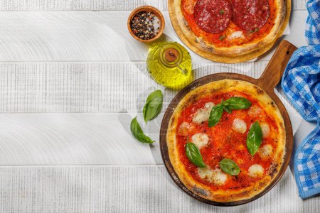 Téléchargez les photos : Pizza maison au margarita et pepperoni, garnie de tomates fraîches, de fromage mozzarella et de feuilles de basilic aromatiques. Sur la table de jardin extérieure à plat avec espace de copie - en image libre de droit