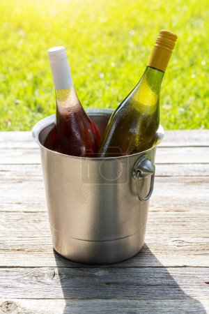 Photo for White and rose wine bottles in ice bucket on an outdoor garden table, setting the scene for a delightful summer party - Royalty Free Image