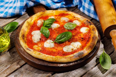 Foto de Pizza de margarita casera, cubierta con tomates frescos, queso mozzarella y hojas aromáticas de albahaca. En la mesa de jardín al aire libre plana con espacio de copia - Imagen libre de derechos