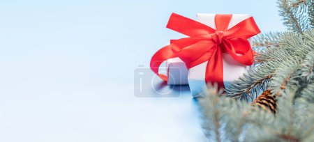Photo for Christmas fir tree branch and gift box over blue background with space for greetings text - Royalty Free Image