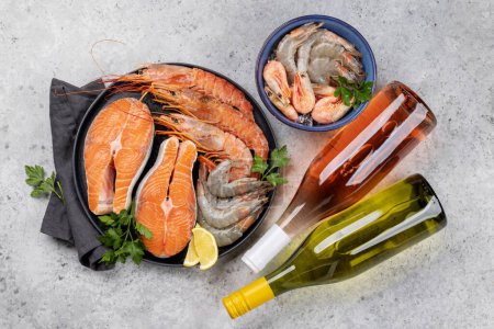 Foto de Una vista superior de mariscos frescos como camarones, langostinos y filetes de trucha, acompañados de vino blanco y rosa - Imagen libre de derechos