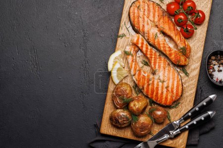 Foto de Filetes de salmón a la parrilla y patatas en una tabla de madera, una delicia deliciosa. Piso con espacio de copia - Imagen libre de derechos