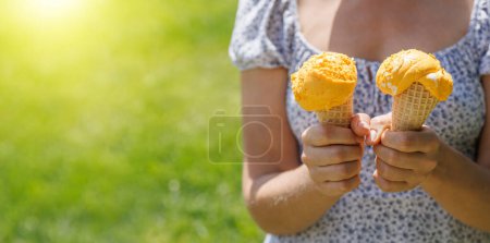 Téléchargez les photos : Les mains de la femme tenant de la crème glacée rafraîchissante dans des cônes de gaufres sont agrémentées d'un soupçon de saveur citronnée. Avec espace de copie - en image libre de droit
