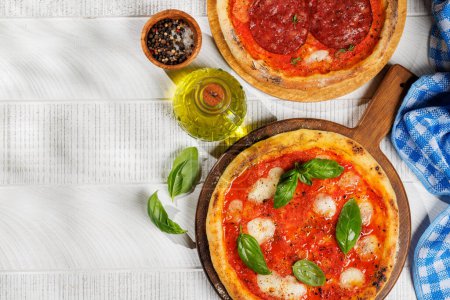 Foto de Pizza casera de margarita y pepperoni, cubierta con tomates frescos, queso mozzarella y hojas aromáticas de albahaca. En la mesa de jardín al aire libre plana con espacio de copia - Imagen libre de derechos