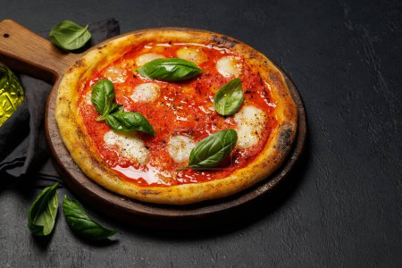Foto de Pizza de margarita casera, cubierta con tomates frescos, queso mozzarella y hojas aromáticas de albahaca - Imagen libre de derechos