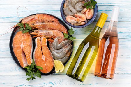 Photo for A top view of fresh seafood such as shrimp, langoustines, and trout steaks, accompanied by white and rose wine - Royalty Free Image