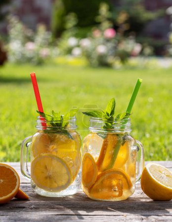 Photo for Refreshing homemade lemonade served on an outdoor garden table. Cold summer drink with fresh citrus fruit and garden mint - Royalty Free Image