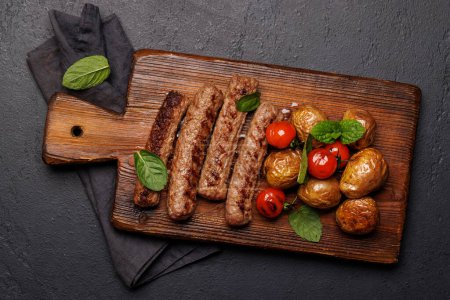 Photo for Delicious grilled sausages and potatoes on a wooden board. Flat lay - Royalty Free Image