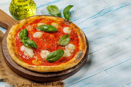 Foto de Pizza de margarita casera, cubierta con tomates frescos, queso mozzarella y hojas aromáticas de albahaca. En la mesa de jardín al aire libre con espacio de copia - Imagen libre de derechos
