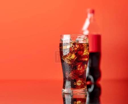Téléchargez les photos : Verre rafraîchissant de cola avec glace et bouteille sur fond. Plus rouge avec espace de copie - en image libre de droit