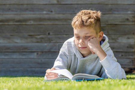 Foto de Un chico leyendo un libro en un campo de hierba. Piso con espacio de copia - Imagen libre de derechos