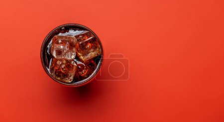 Téléchargez les photos : Verre rafraîchissant de cola avec glace. Sur fond rouge avec espace de copie. Pose plate - en image libre de droit