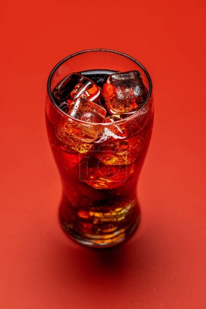 Téléchargez les photos : Verre rafraîchissant de cola avec glace. Sur fond rouge - en image libre de droit