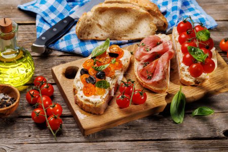 Téléchargez les photos : Un délicieux ensemble sandwich de bruschetta orné de tomates juteuses, de fromage et de prosciutto salé sur la table de jardin extérieure - en image libre de droit