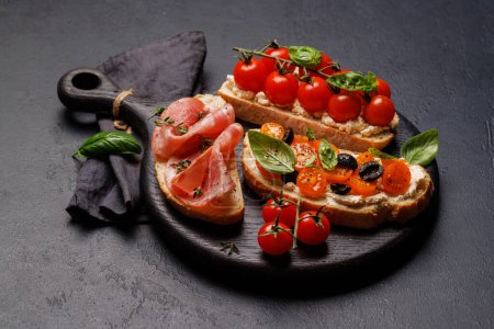 Foto de Un delicioso sándwich de bruschetta adornado con jugosos tomates, queso y salado prosciutto - Imagen libre de derechos