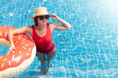 Photo for Beautiful young woman with inflatable donut ring relaxing in swimming pool. Summer vacation. With copy space - Royalty Free Image