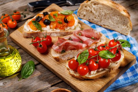 Téléchargez les photos : Un délicieux ensemble sandwich de bruschetta orné de tomates juteuses, de fromage et de prosciutto salé sur la table de jardin extérieure - en image libre de droit