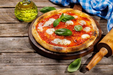 Foto de Pizza de margarita casera, cubierta con tomates frescos, queso mozzarella y hojas aromáticas de albahaca. En la mesa de jardín al aire libre - Imagen libre de derechos