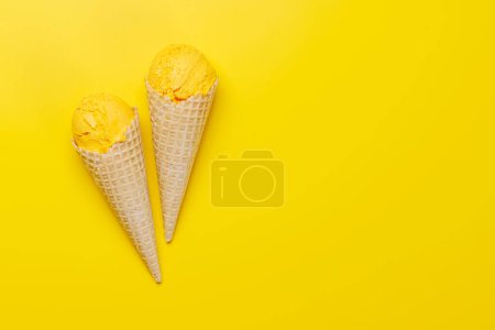 Téléchargez les photos : Glace au citron dans de délicieux cônes de gaufres, un régal pour tous les papilles. Sur fond jaune avec espace de copie, pose plate - en image libre de droit